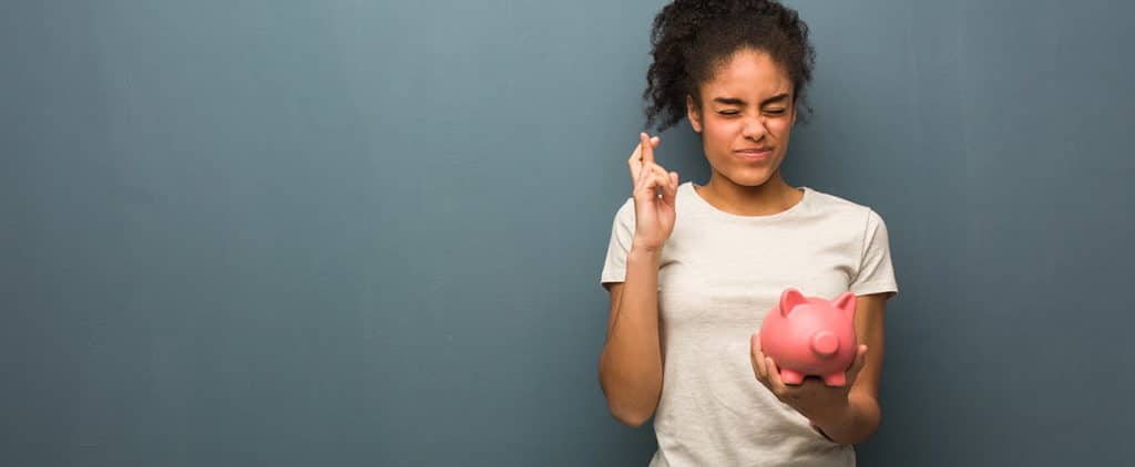 Woman crosses fingers while holding piggy bank