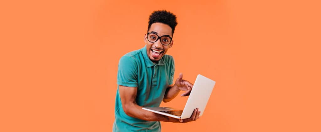 Student with glasses smiling and pointing at laptop