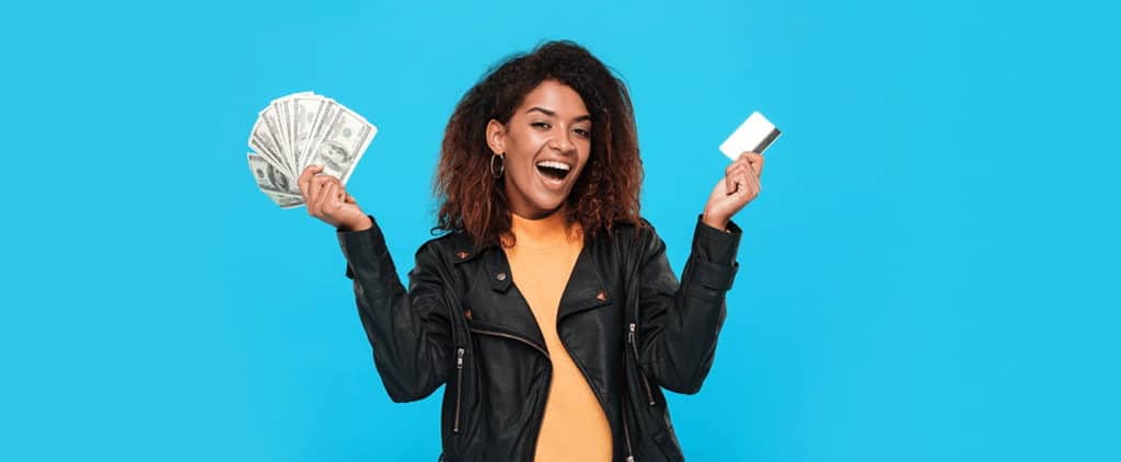 Woman in jacket holding one credit card in her hand and cash in the other hand