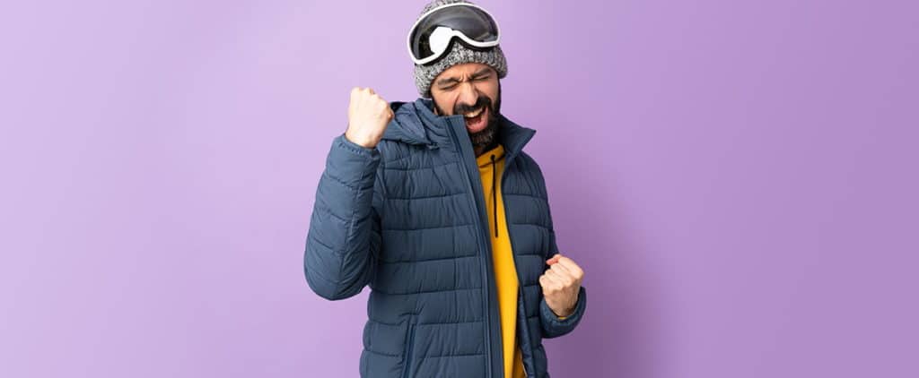 Excited man pumping fists wearing snow jacket and goggles