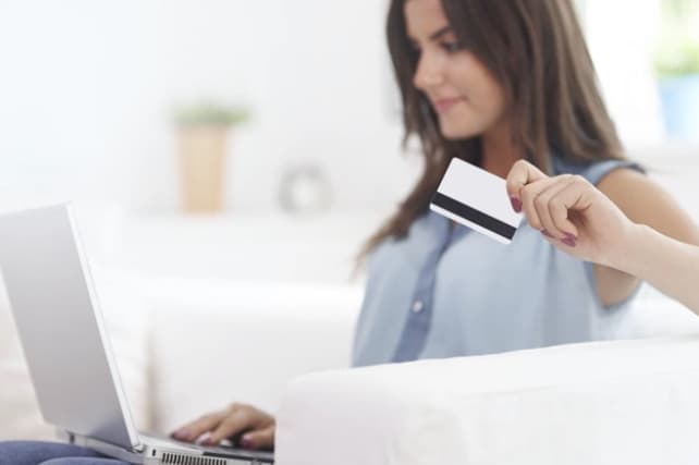 Woman holding credit card while looking at laptop